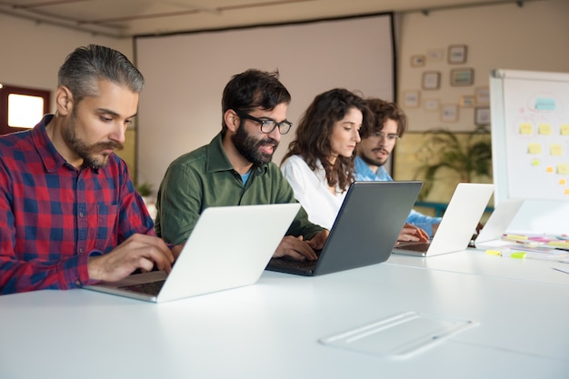 Startup team collaborating on project, using laptops